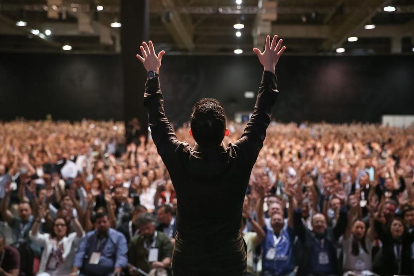 a man holding his hands up in front of a large crowd audible range volume point happen singing excellent post good posture visual representation mouth mouth speech microphone speaking microphones microphone