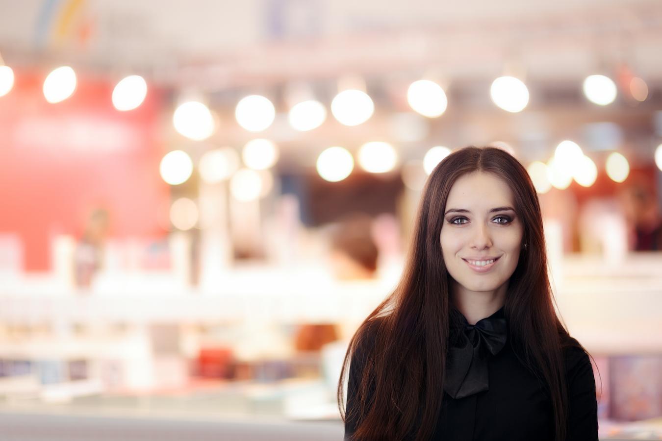 Event planner in a black blowed blouse stands at a venue with warm lights and smiles at the camera