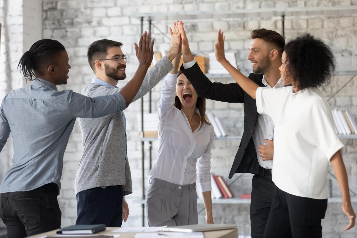 Five team members demonstrate the importance of team building as they high five in the office