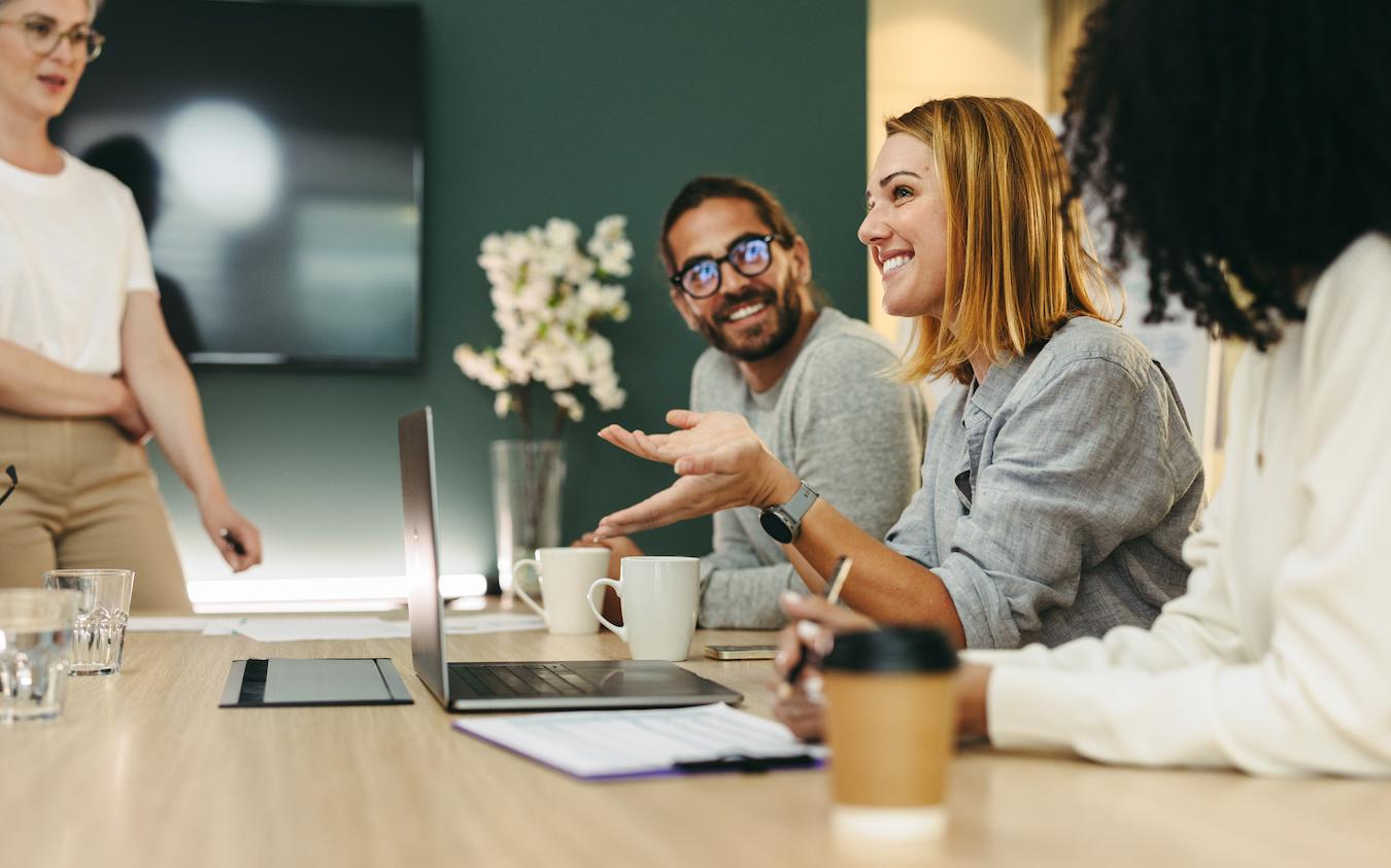 Four business colleagues sit at a table and smile as they talk about their weekends and shared hobbies