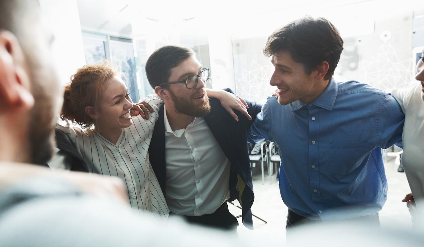 Four people stand in circle with arms around each other smiling and expressing appreciation for each other