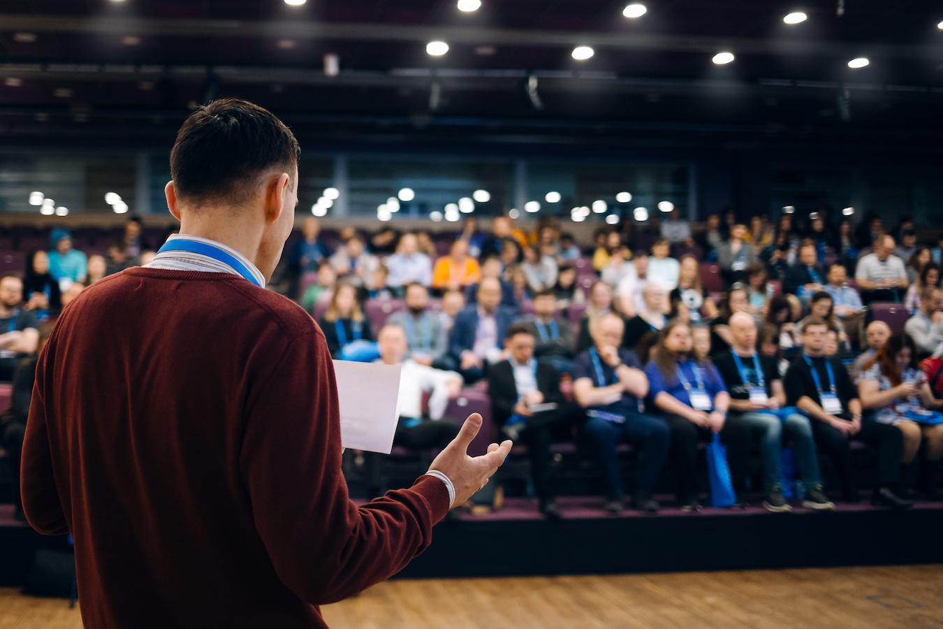 Host on stage keeps things moving and looks at notes to introduce guests making speeches