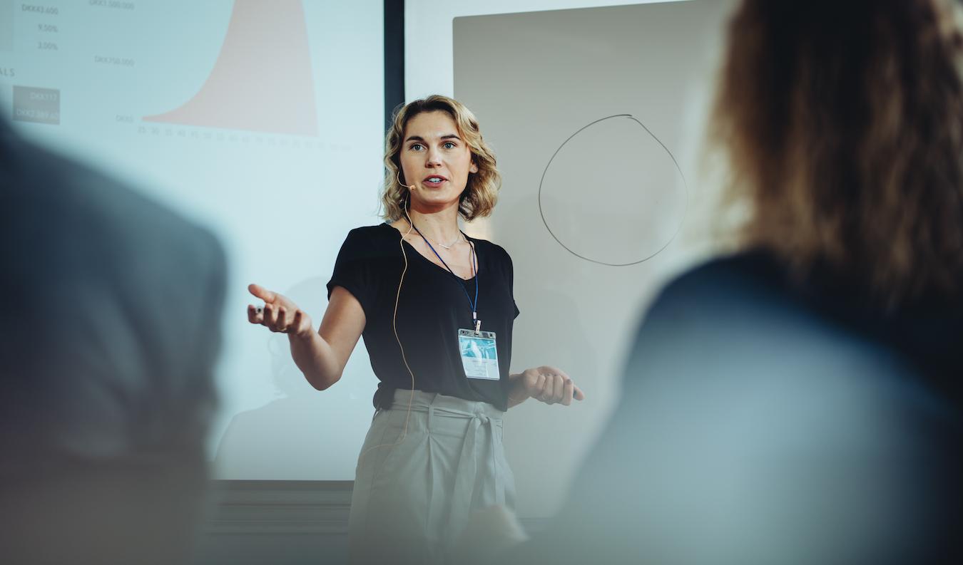Lone speaker on stage makes gesture toward audience while making a point during presentation