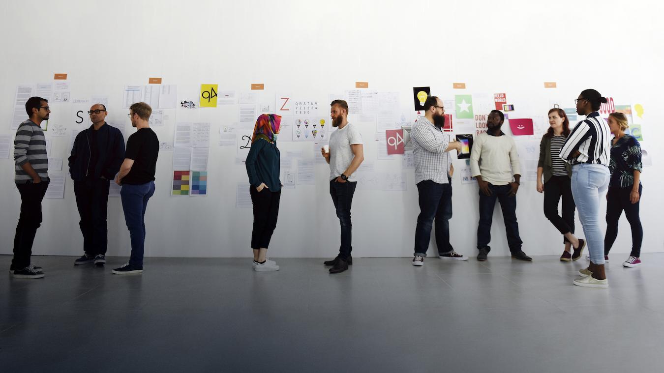 People mingle at an event in front of a white wall with posters