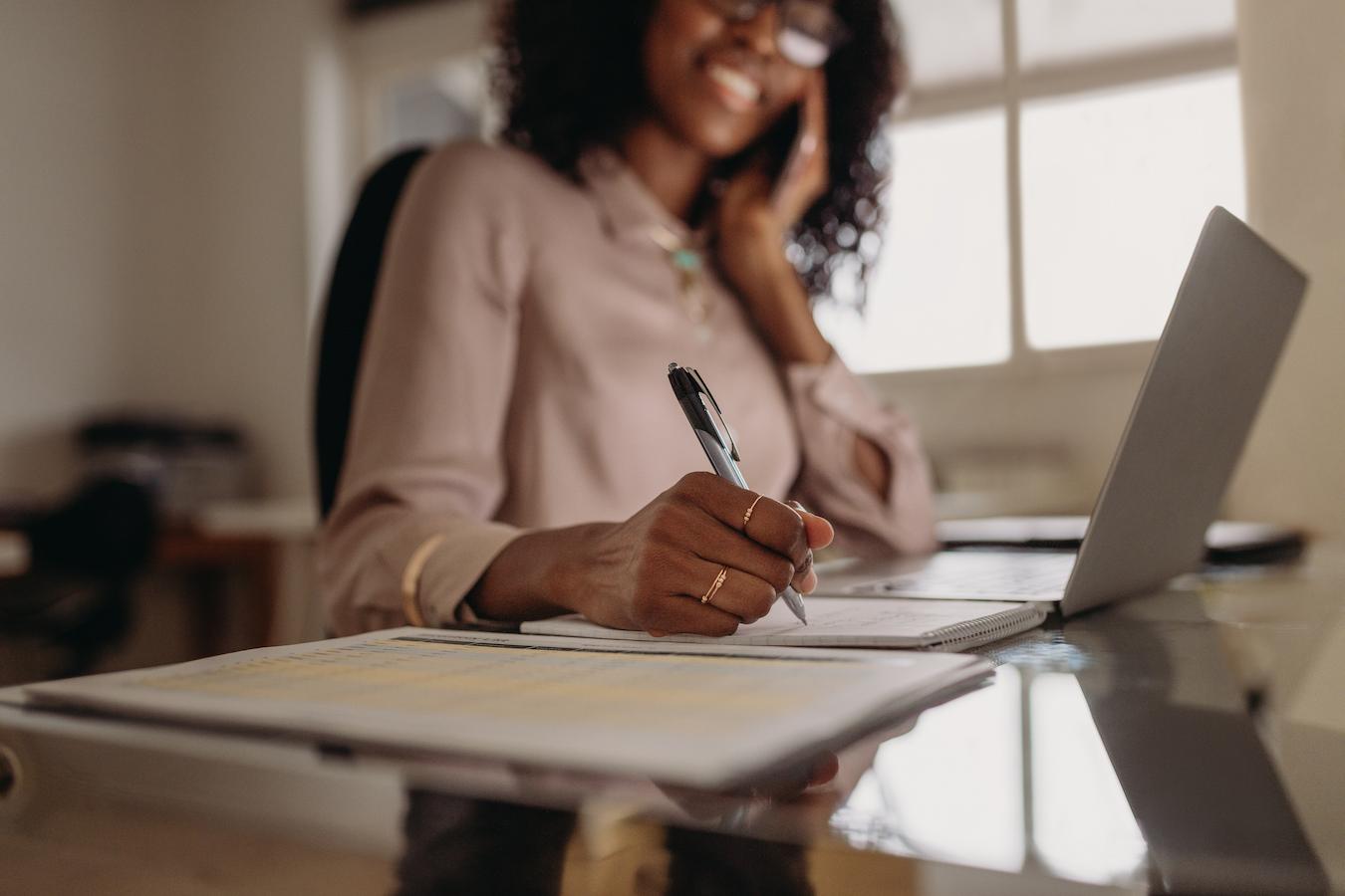 Person in blush blouse wearing gold rings writes meeting agenda examples as part of their meeting agenda template business
