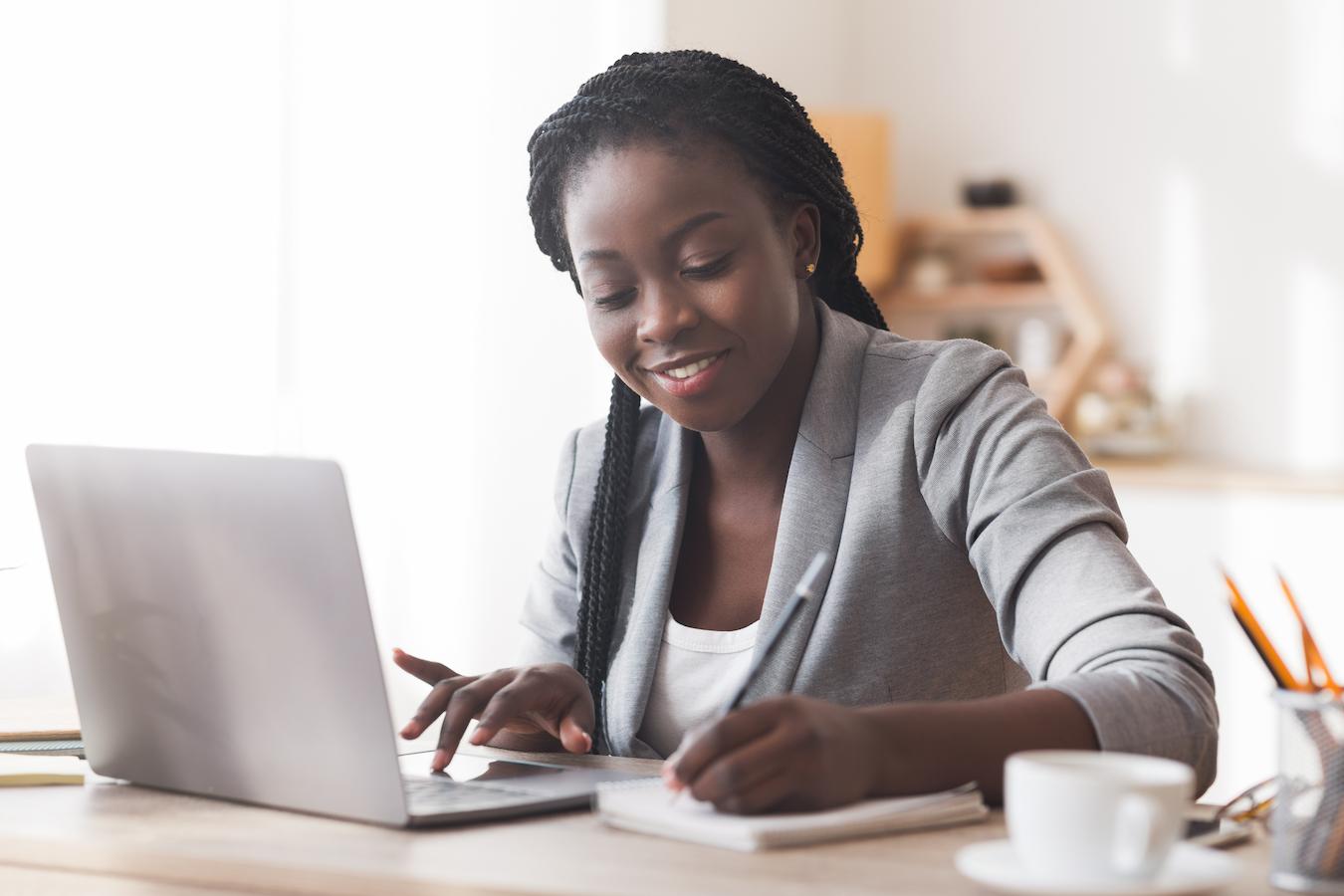 Person in gray blazer sits in front of a laptop and practices good time management skills by writing in their planner
