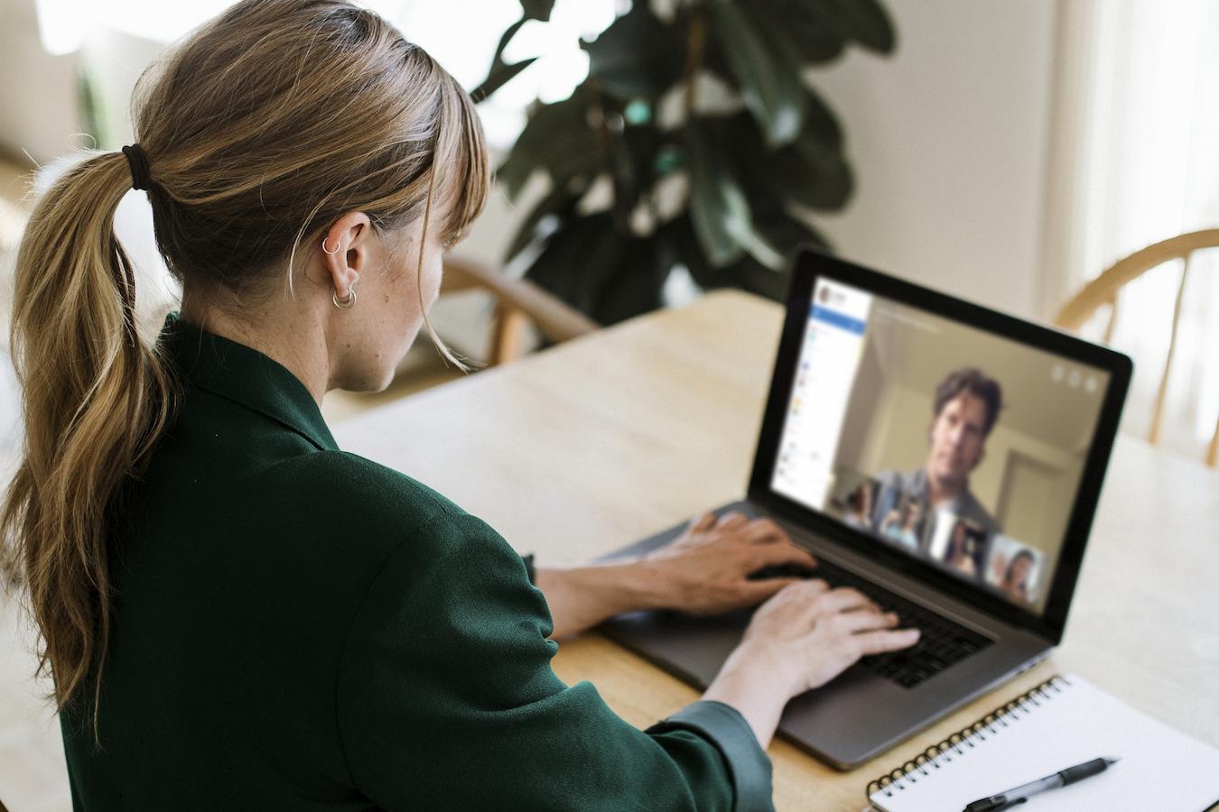 Person in green blazer sits at table and participates in video conference with employees