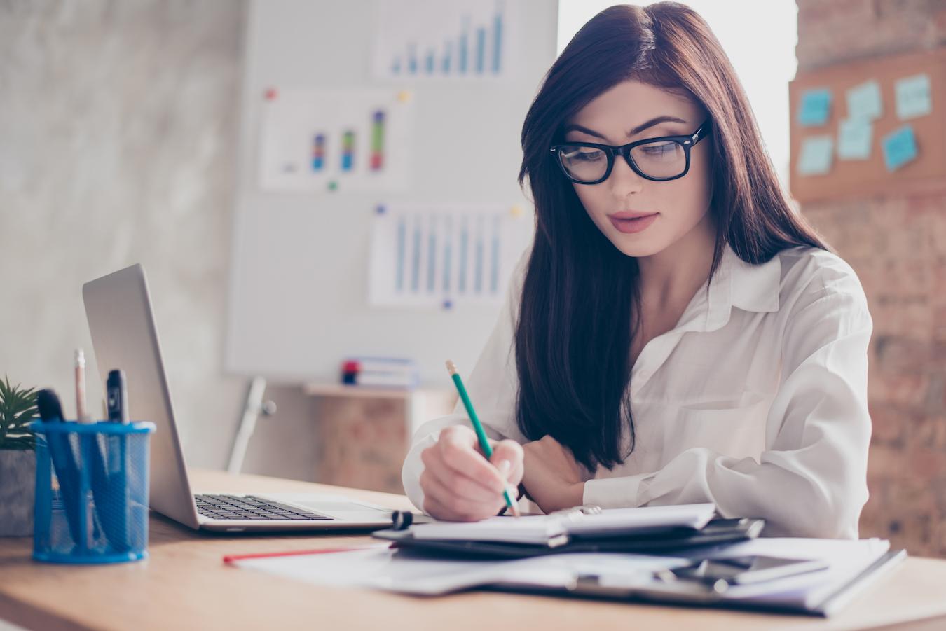 Person in white blouse who plans events for business clients sits at a desk and plans out their calendar of upcoming events