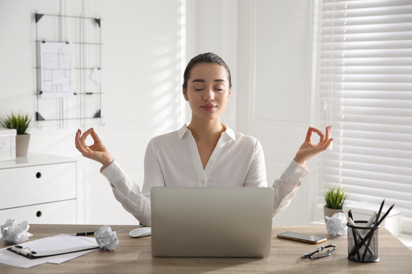 Person in white button down stays calm at their desk by breathing and practicing meditation which keeps their head clear during stressful times in life
