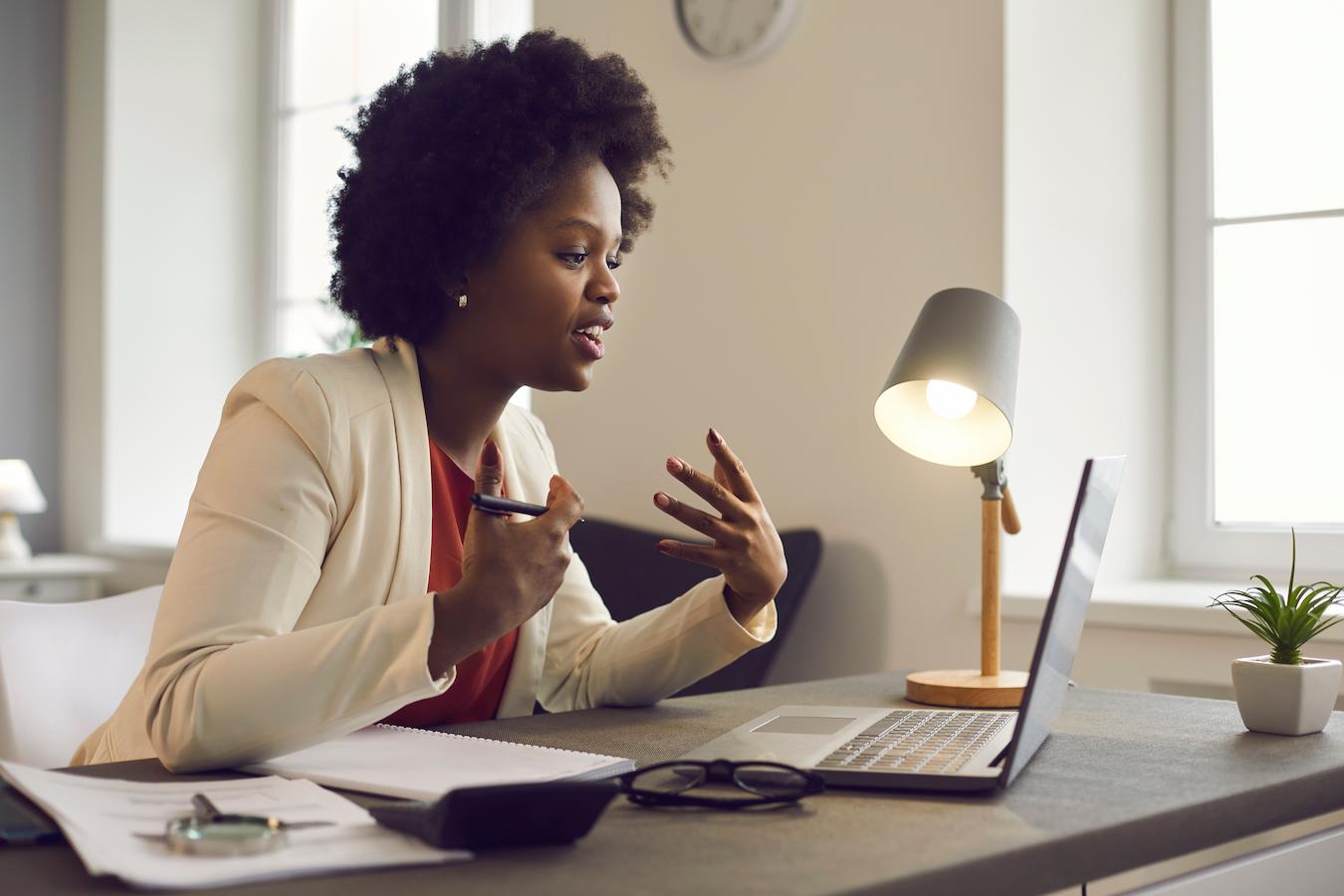 Person sits at desk and speaks words on video call to make a point that colleagues listen to in preparation for big meeting