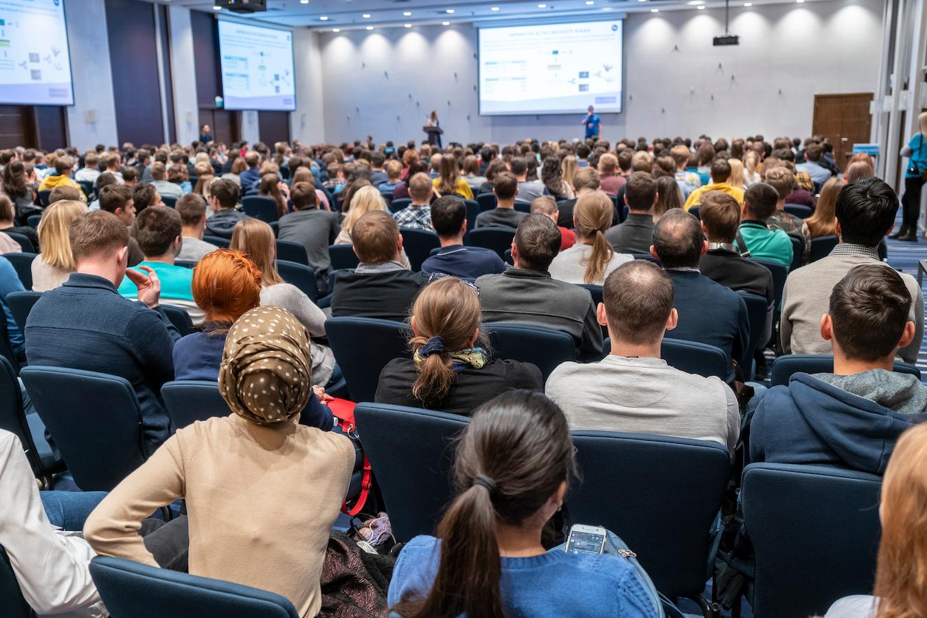Room of attendees listen to speakers talk on stage