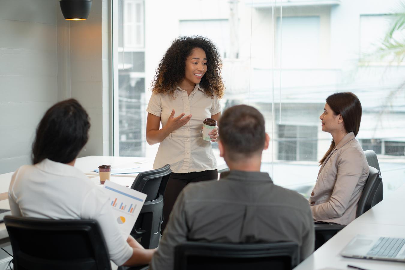 Team of four people in a sunny office use a meeting agenda template to answer questions in their team meetings