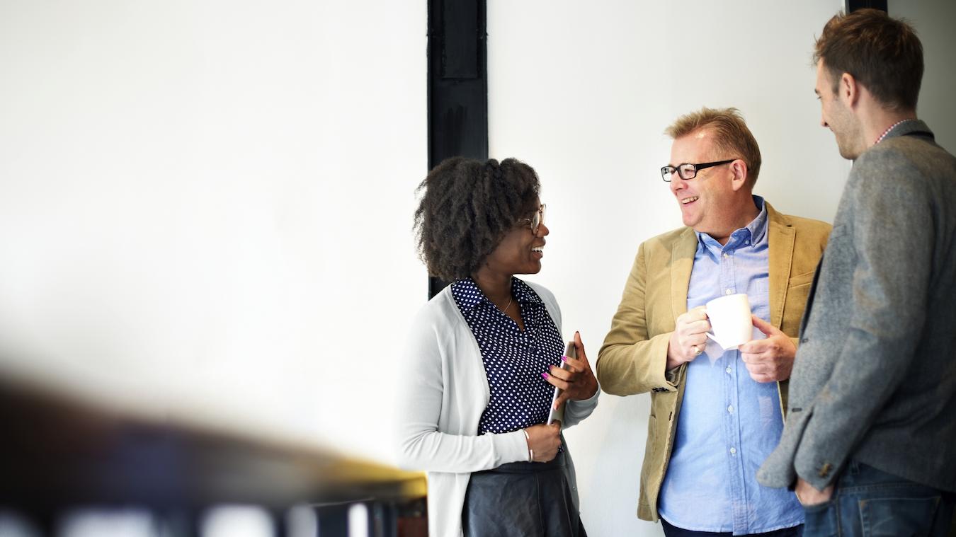 Three coworkers stand and chat with each other over coffee