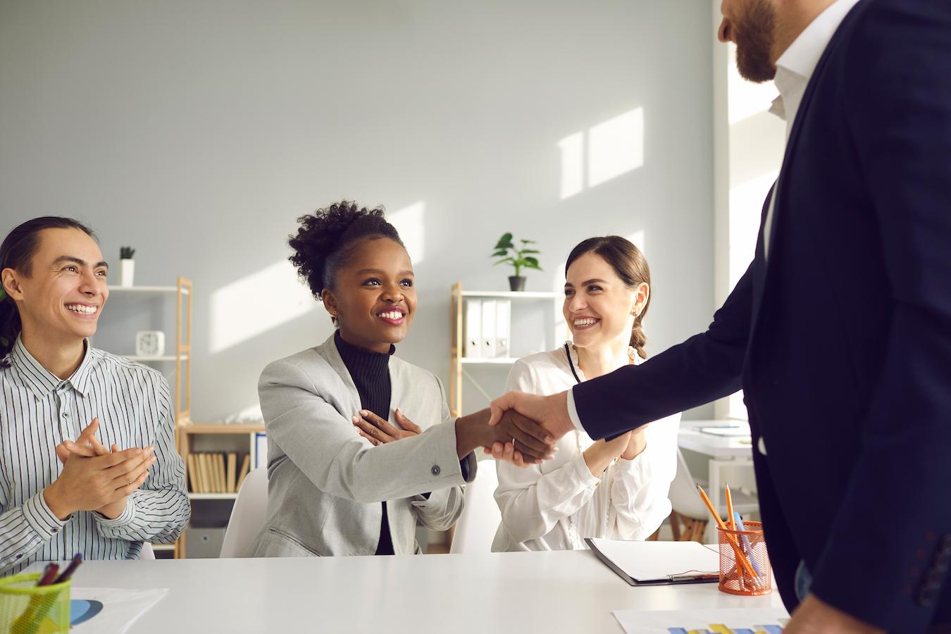 Three people maintaining rapport with each other for years smile as one shakes hands with a client strong connection and a positive work process