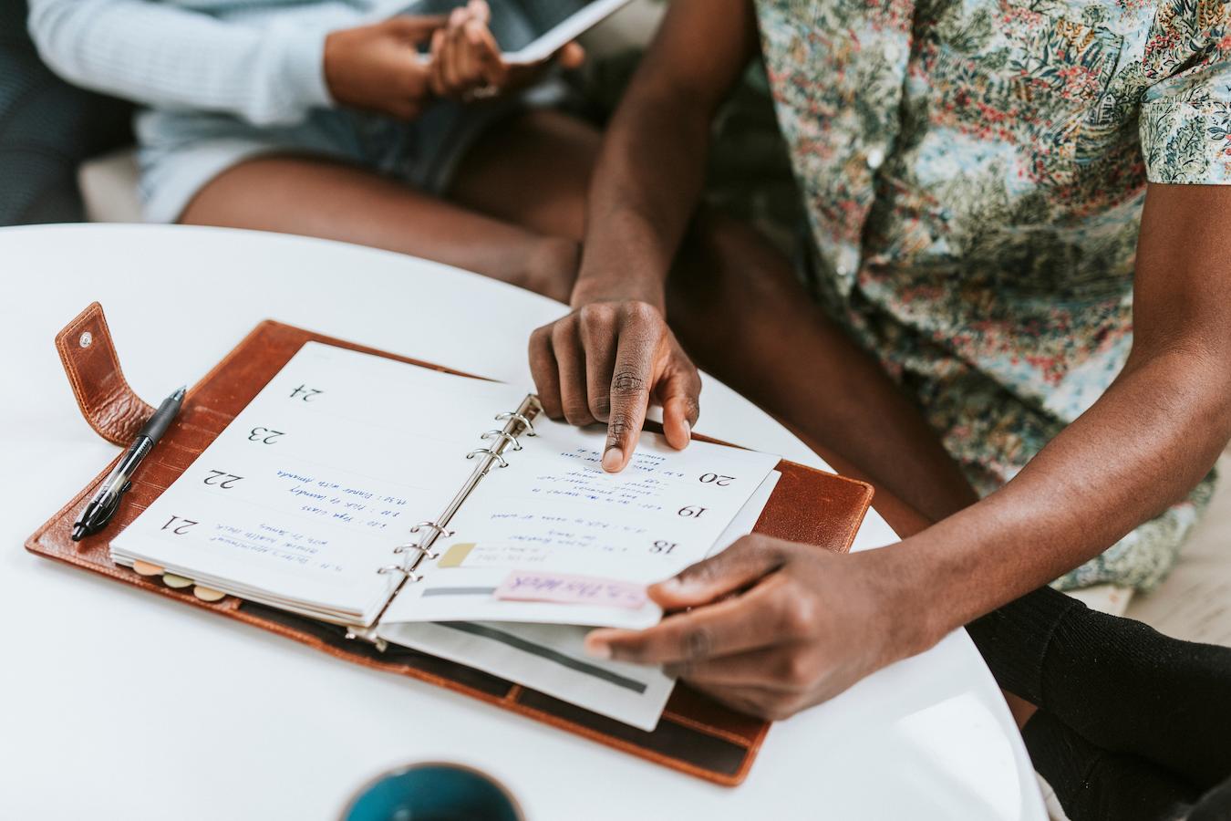 Two event planner coordinate their schedule of business meetings regarding an upcoming public relations campaign